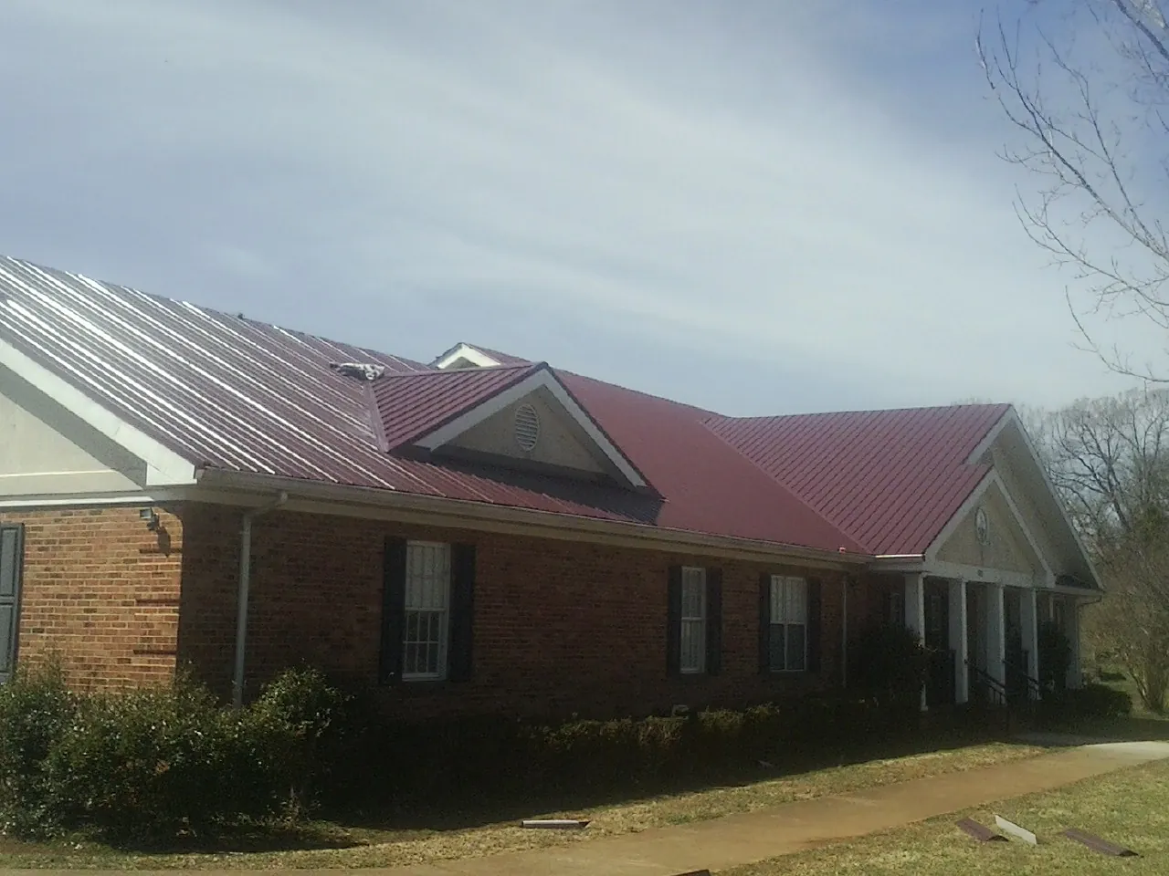 Red metal roof with gabled entries on a long brick building, from a Hail Damage Roof Repair job in Casco
