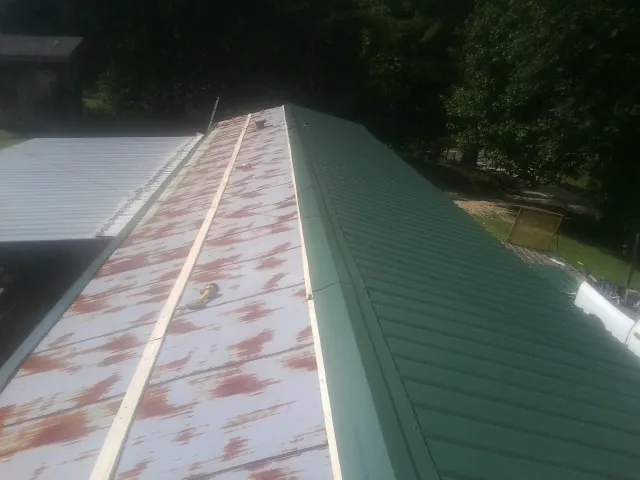 Old rusted panels beside newly installed green metal roofing — Wind Damage Roof Repair by Roofing Brothers in Casco