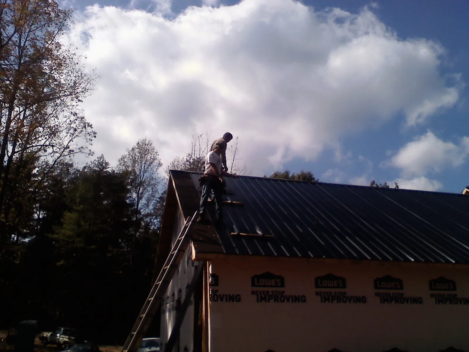 Roofer fastening dark metal panels high against a cloudy sky, from a Roof Inspection job in Casco