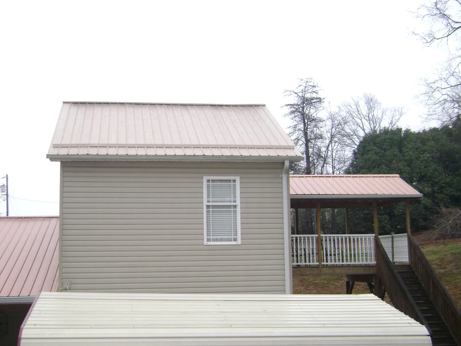 Tan metal roofs on a two story addition and attached porch, from a Roof Replacement job in Casco